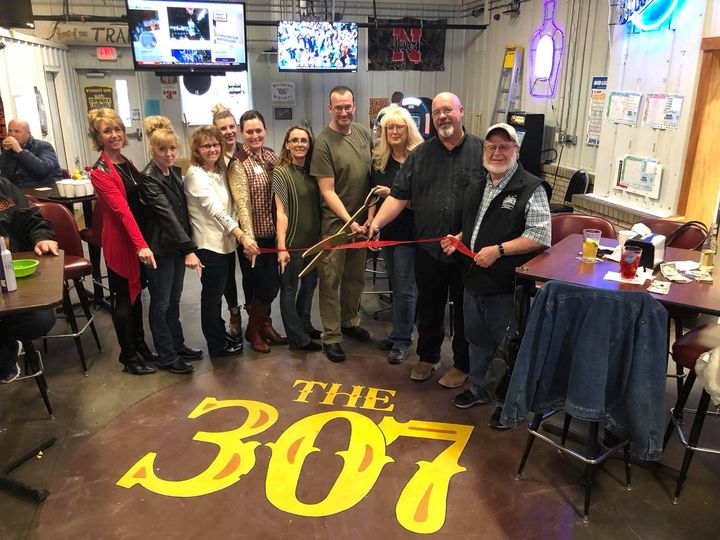 a group of people standing around a red ribbon in a restaurant. One man has a large pair of scissors