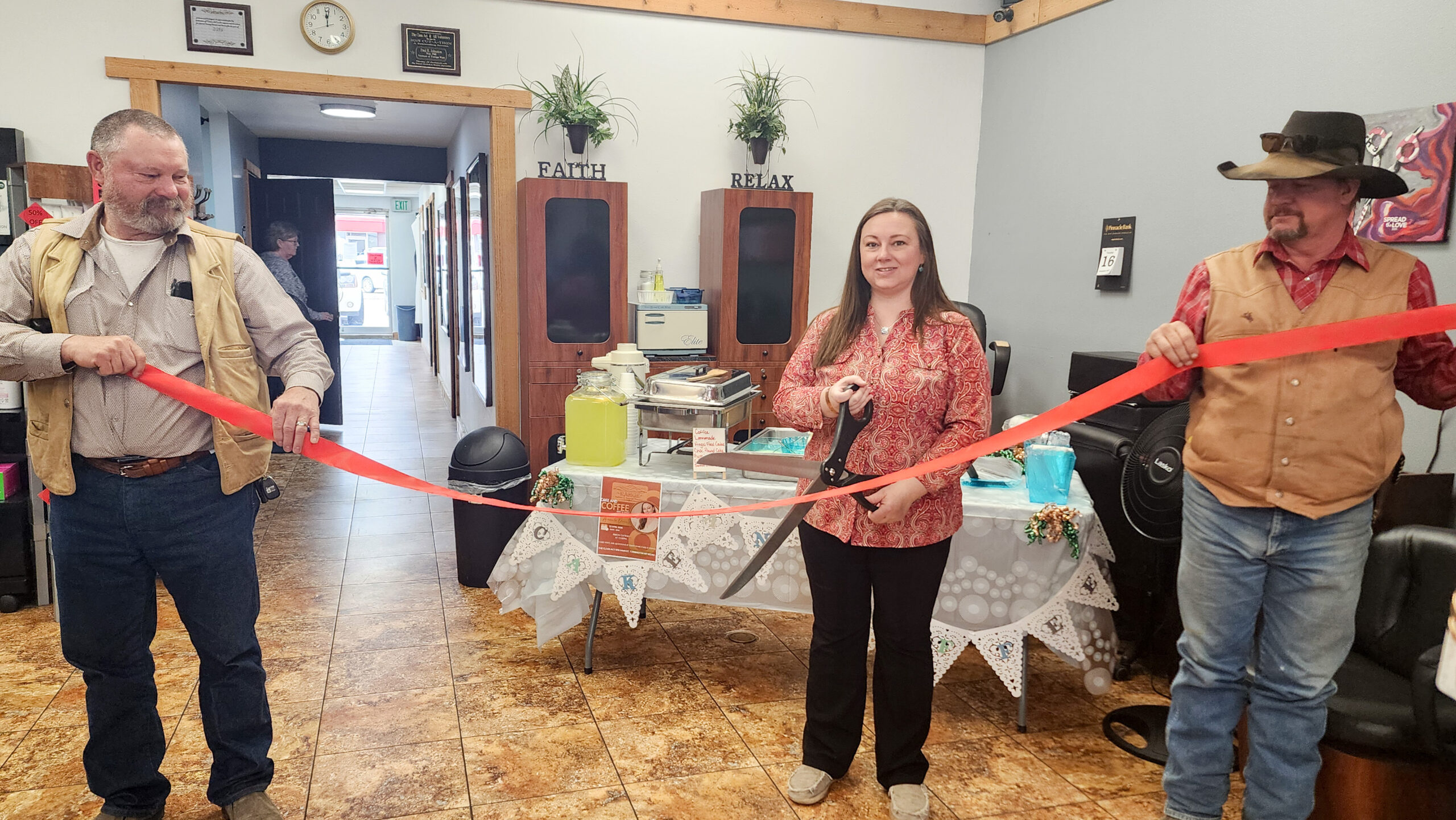 Amanda Dennis stands in the center cutting a red ribbon during the grand opening of Range Wellness & Massage Therapy at The Class Act in downtown Torrington, while two family supporters hold the ribbon on each side.